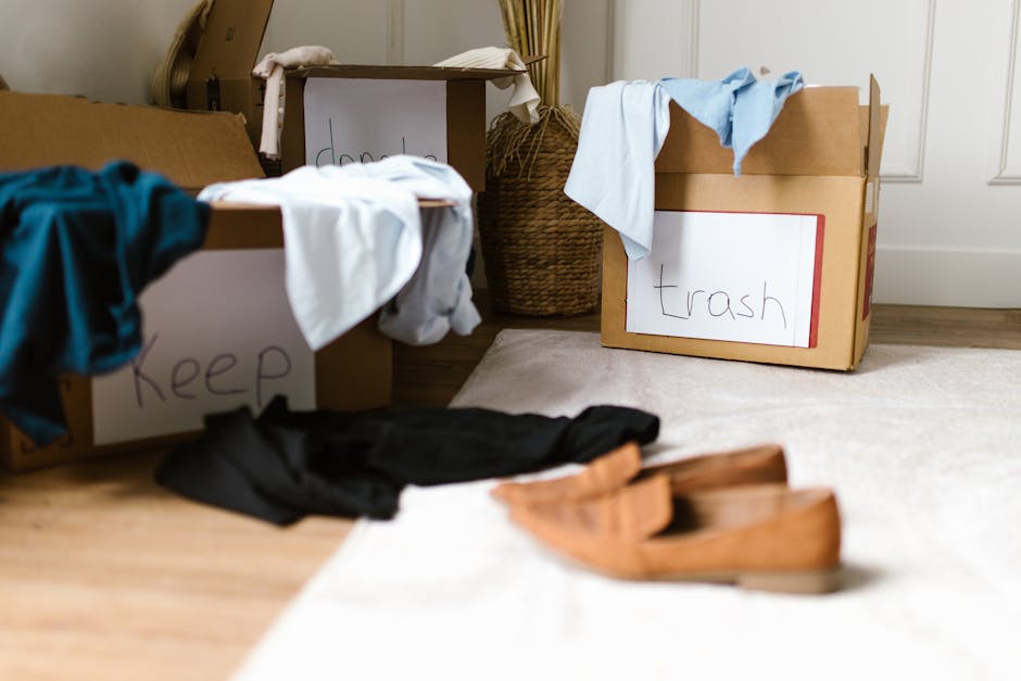 The image depicts a room under renovation or preparation for clearance, with various waste and materials spread across a light-colored floor. Prominently visible are several cardboard boxes, some open